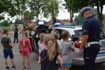 Dzieci ustawione obok radiowozu policyjnego oglądają urządzenie do pomiaru prędkości prezentowane przez policjanta.