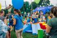 Na zewnątrz stoją dorośli i dzieci bawiące się kolorowymi zabawkami. W tle widać kolorowe baloniki i niebieski namiot z napisem 500+