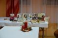 Na stole z białym obrusem ułożono kilkadziesiąt książek. Na pierwszym planie na innym stole jest stroik świąteczny z czerwonym świec.