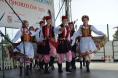 Grupa tancerzy w krakowskich strojach ludowych tańczy na plenerowej scenie