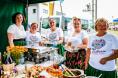 Pięć kobiet w strojach ludowych pozuje do zdjęcia wokół stojąc obok stołu z jedzeniem