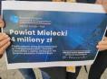  Tablica trzymana w dłoniach z napisem: Powiat Mielecki otrzymał 4 miliony zł na zadanie Przebudowa dróg powiatowych.